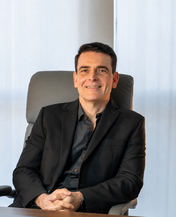 Dr. Marcelo Bianchin sentado em seu consultório, de terno escuro